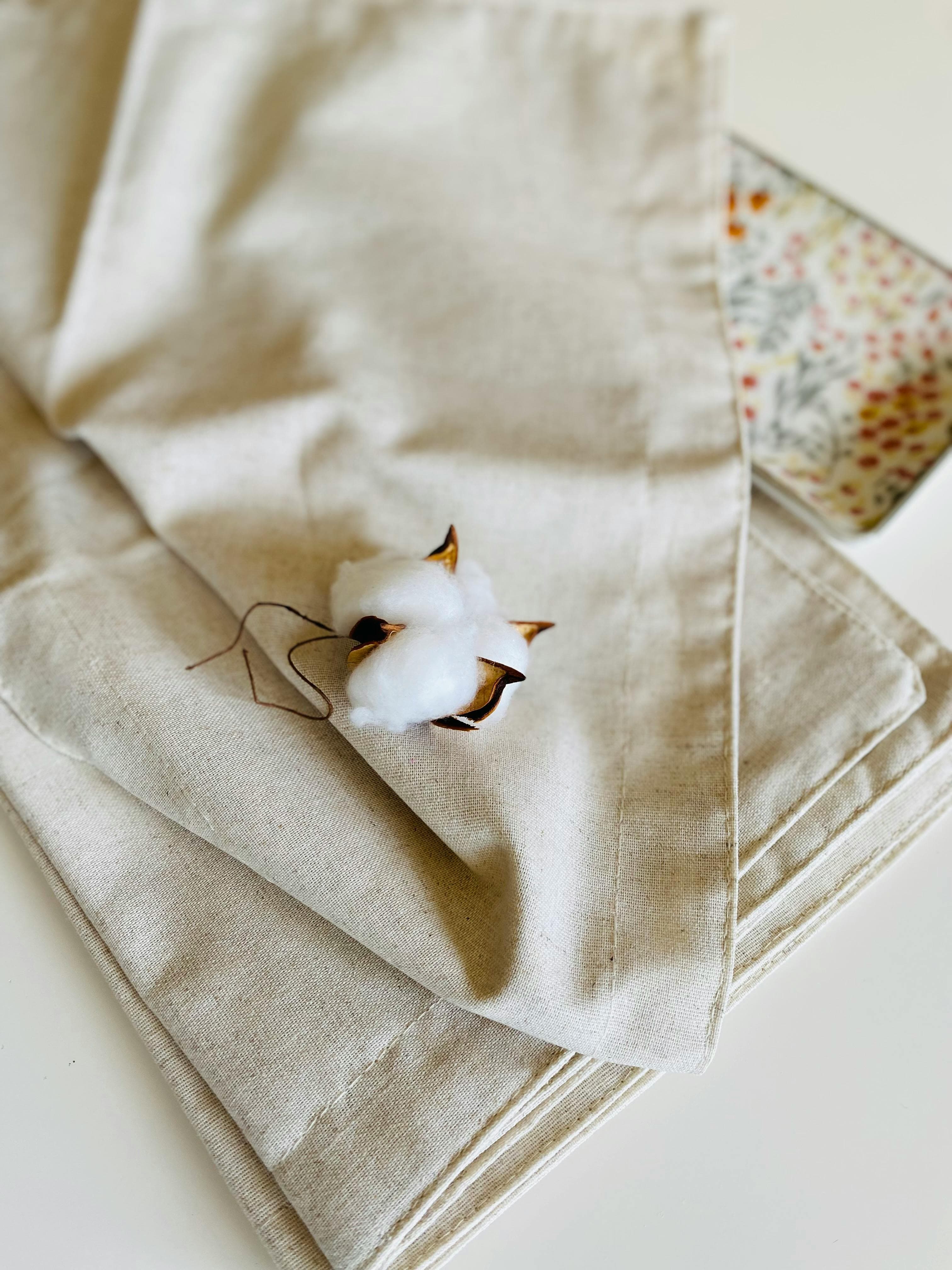 A single cotton boll resting on beige linen — a study of natural fibre.