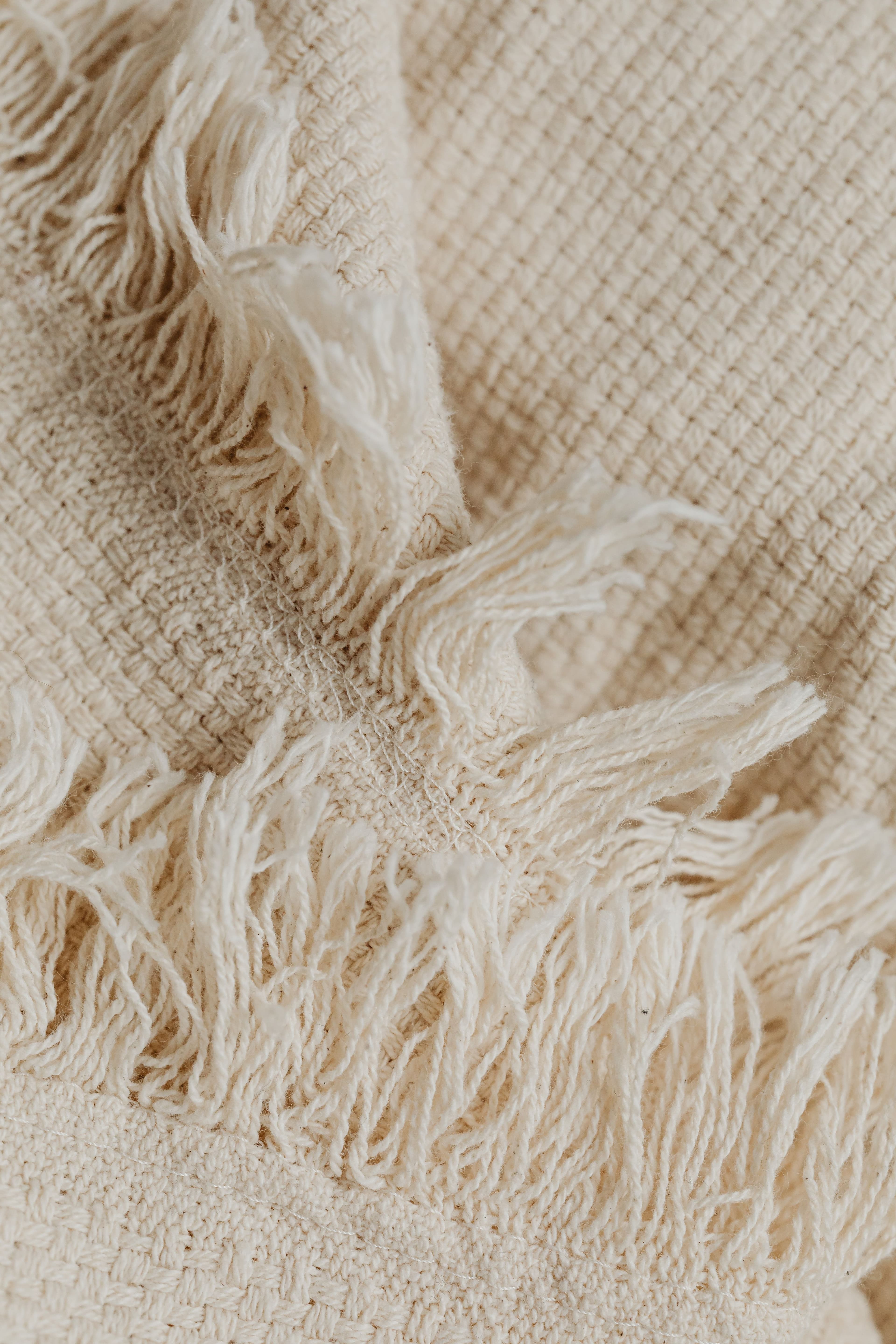 Détail d’un textile beige à franges, montrant un bord tissé à la main.